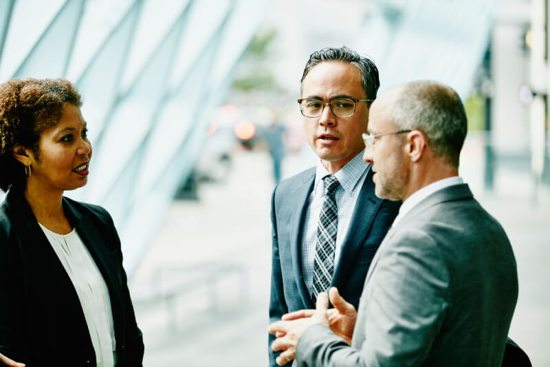 Three colleagues in discussion in outdoor corridor of office building